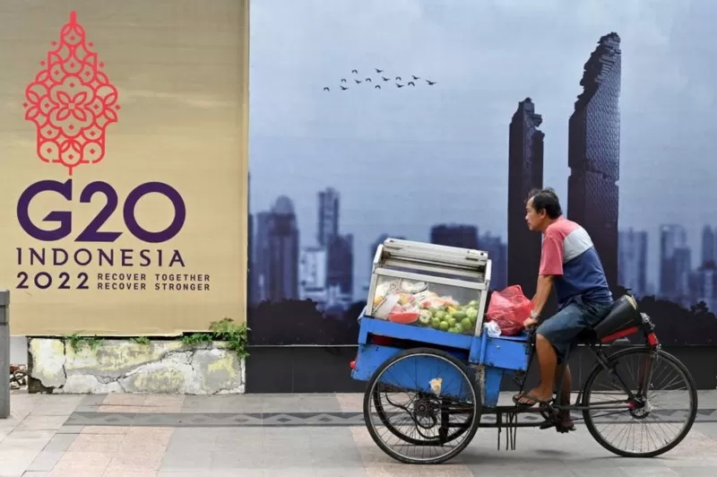 A fruit vendor rides his cart past a logo of the G20 Summit